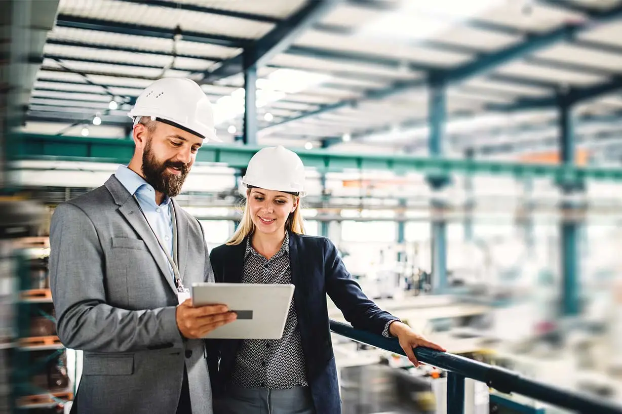 A smiling man and woman in a warehouse looking at a tablet to confirm everything is on track