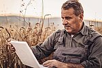 A farmer in a field checking his laptop to make sure transportation is running smoothly 